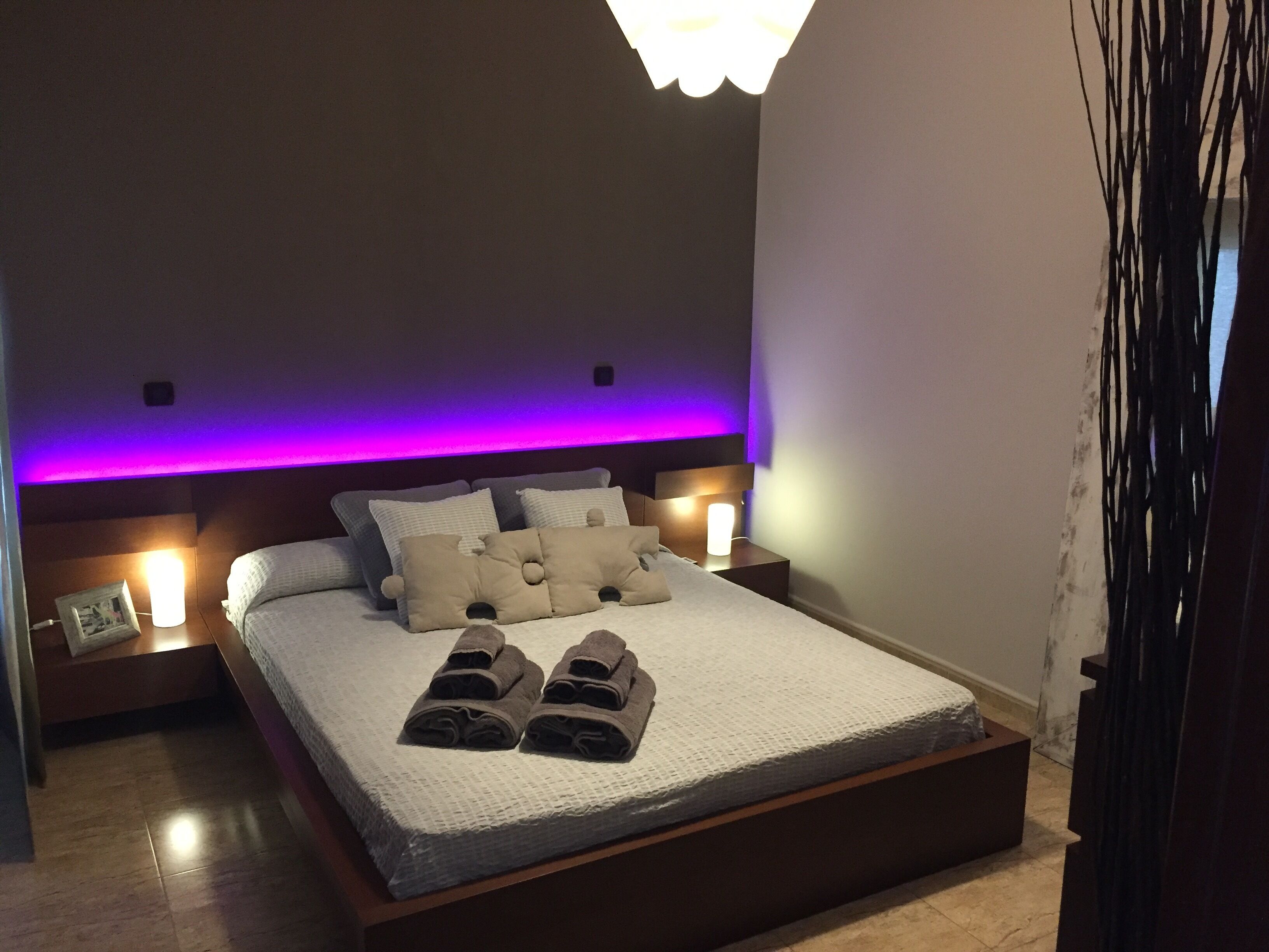 Une chambre à coucher avec un lit, des oreillers, une table de chevet et un luminaire fixé au mur.