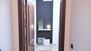 A hallway with a wooden door, a black textured wall, a small shelf with a lamp, and a motivational sign on the floor.