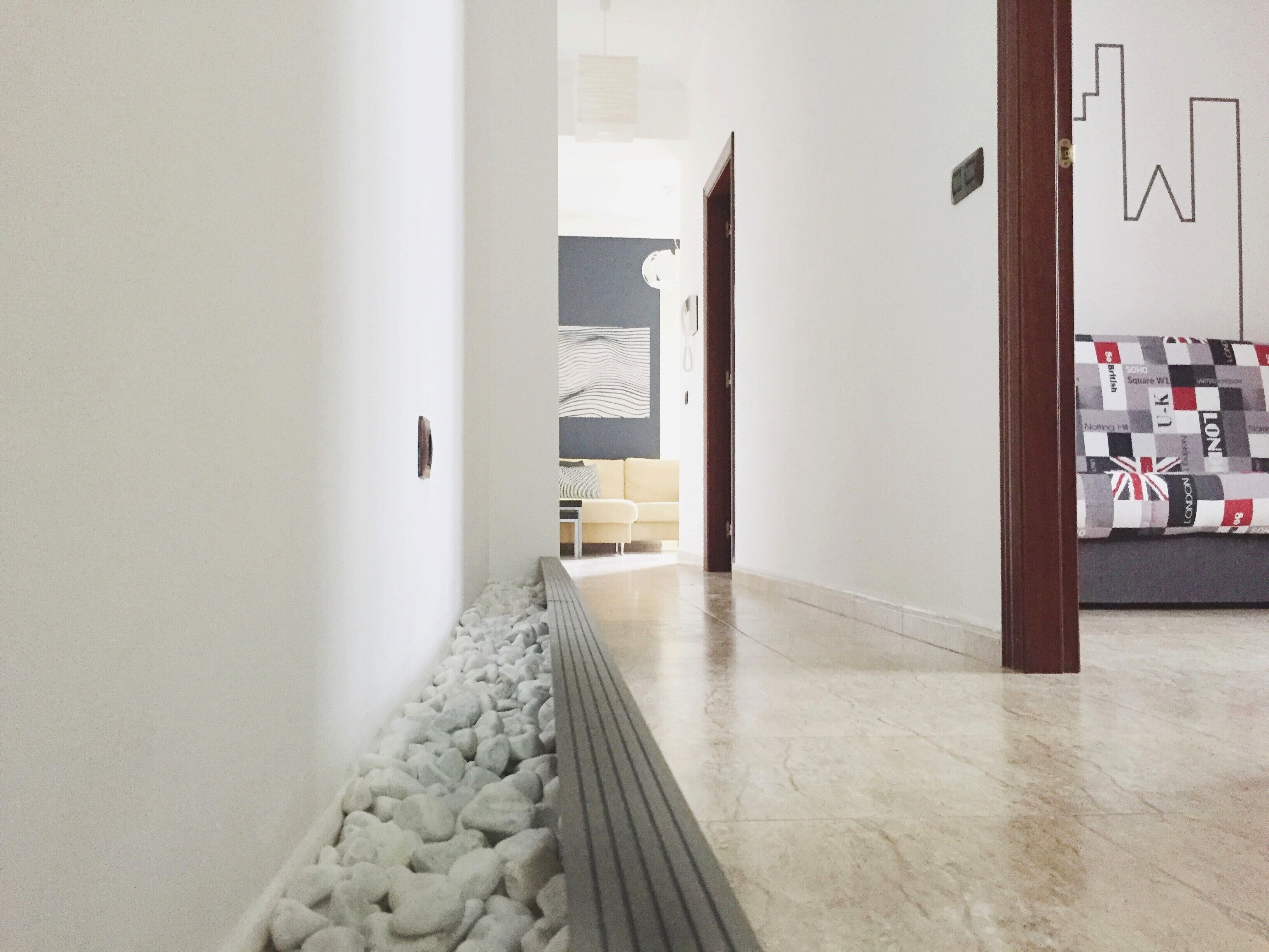 Un pasillo con suelo de guijarros, un sofá con funda estampada y una puerta que da a otra habitación.