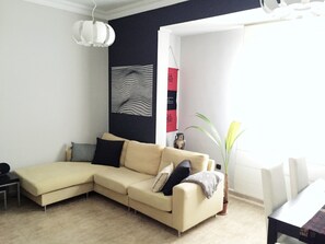 A living room with a beige sectional sofa, a small table, a potted plant, and a wall with abstract art. - NEXT TO LAS CANTERAS BEACH! Lovely and spacious apt. 80 m2 well located (Las Palmas de Gran Canaria)