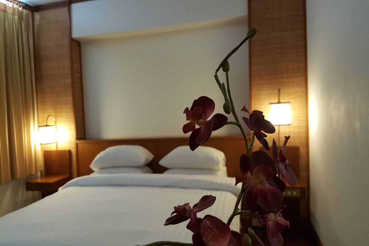 Una habitación de hotel con una cama, dos lámparas de noche y una orquídea en maceta.