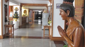 A hallway with a statue, wooden furniture, and a refrigerator. - Dusit Hotel at Sakon Nakhon (Sakon Nakhon)