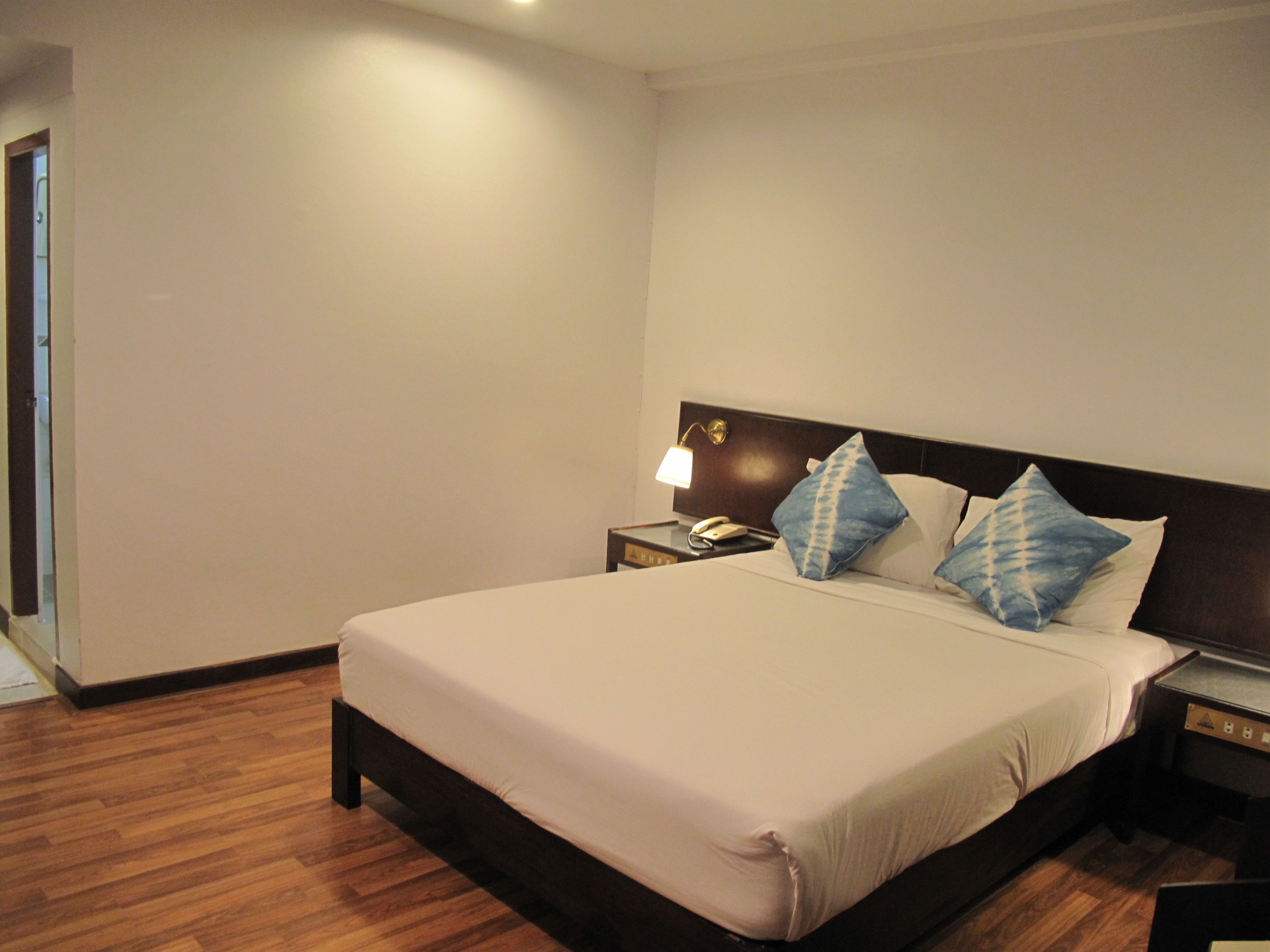 Una habitación de hotel con una cama grande, suelo de madera, una mesita de noche con lámpara y teléfono.