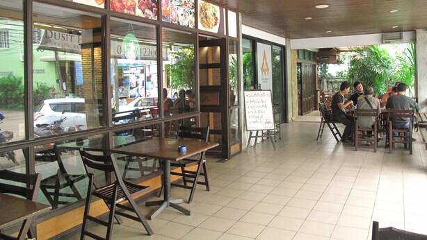 A restaurant with a view of the street, tables and chairs, and a menu board. - Dusit Hotel at Sakon Nakhon (Sakon Nakhon)