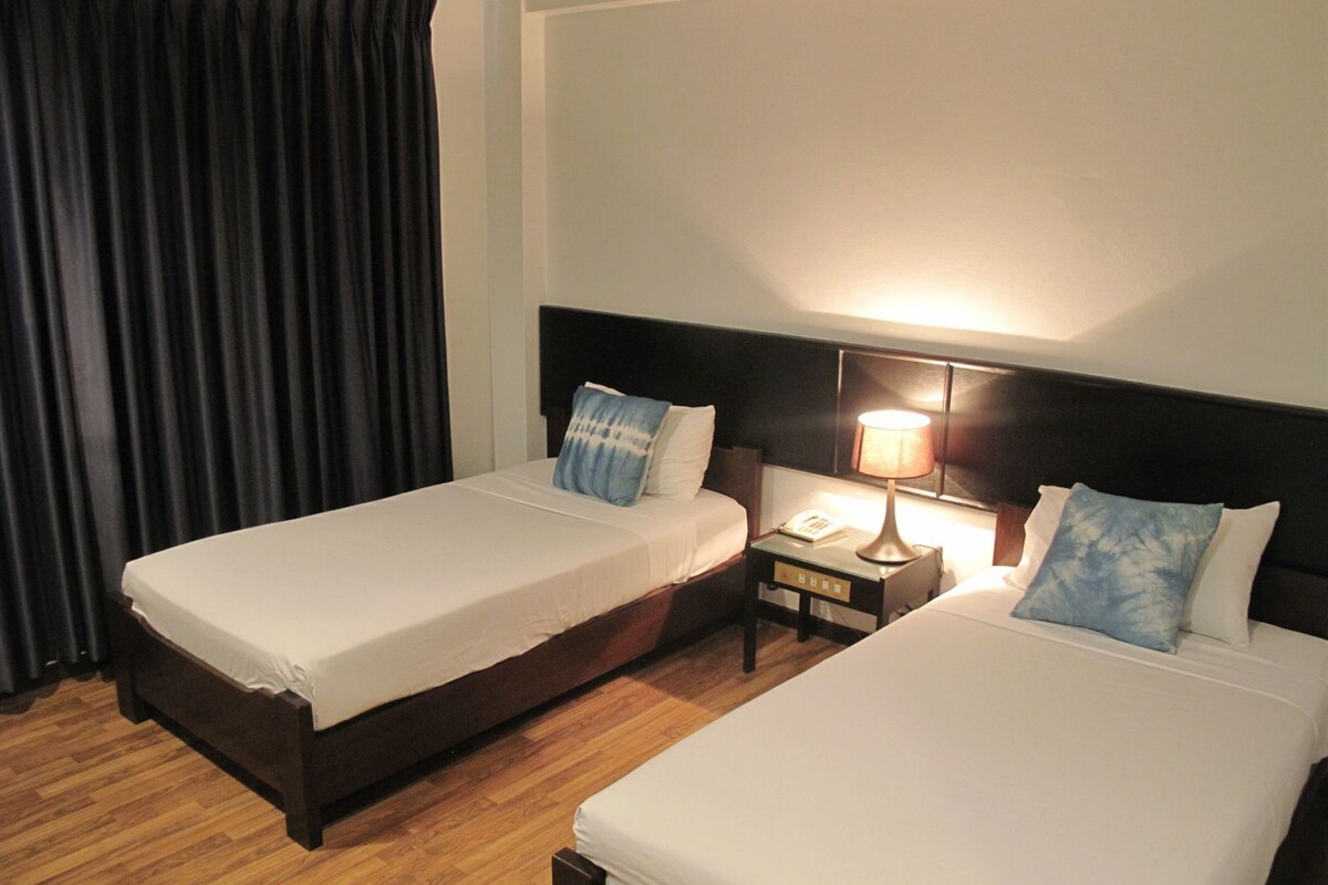 Une chambre d’hôtel avec deux lits, une table de chevet avec une lampe et un rideau.