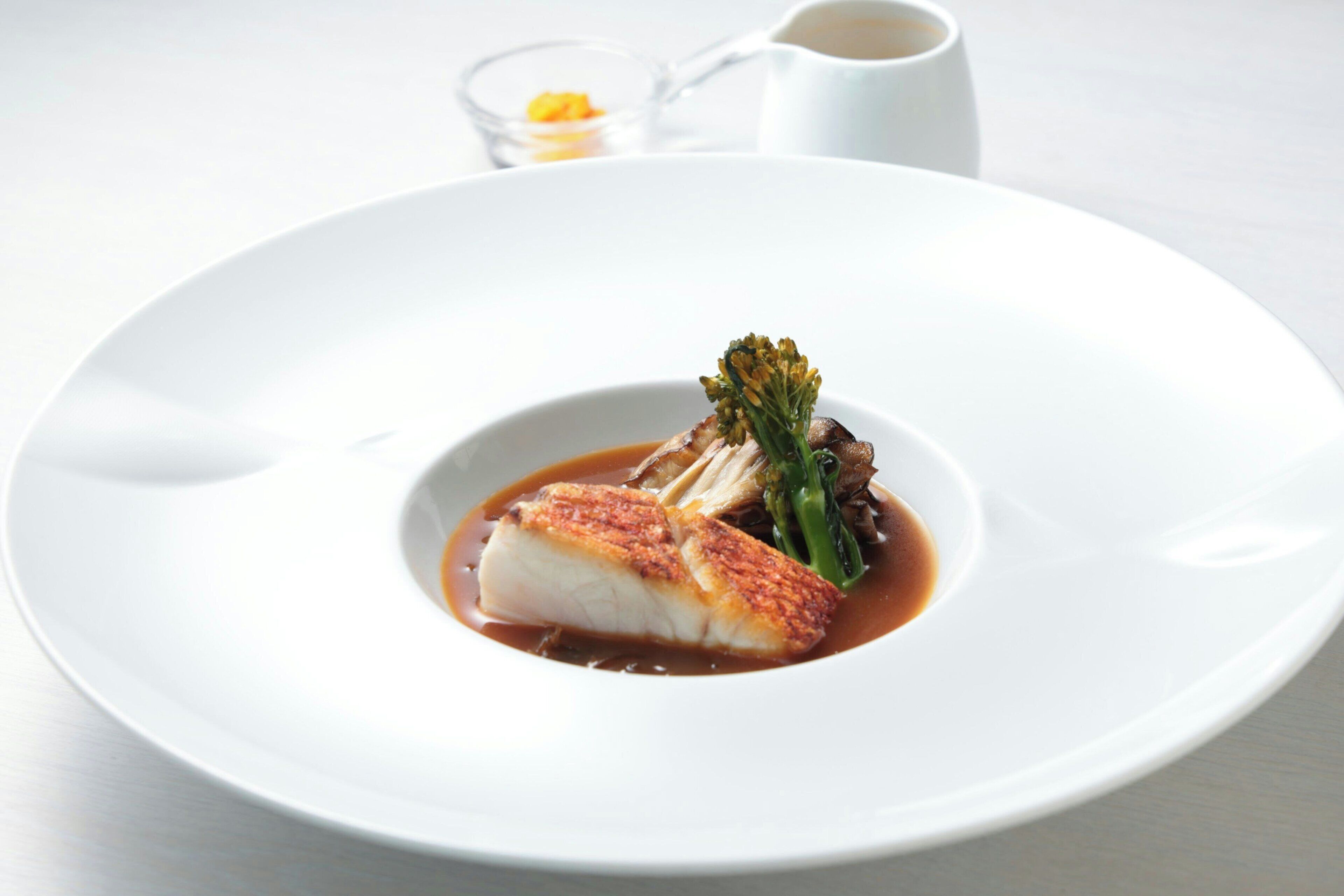 A white plate with a piece of fish, vegetables, and sauce.