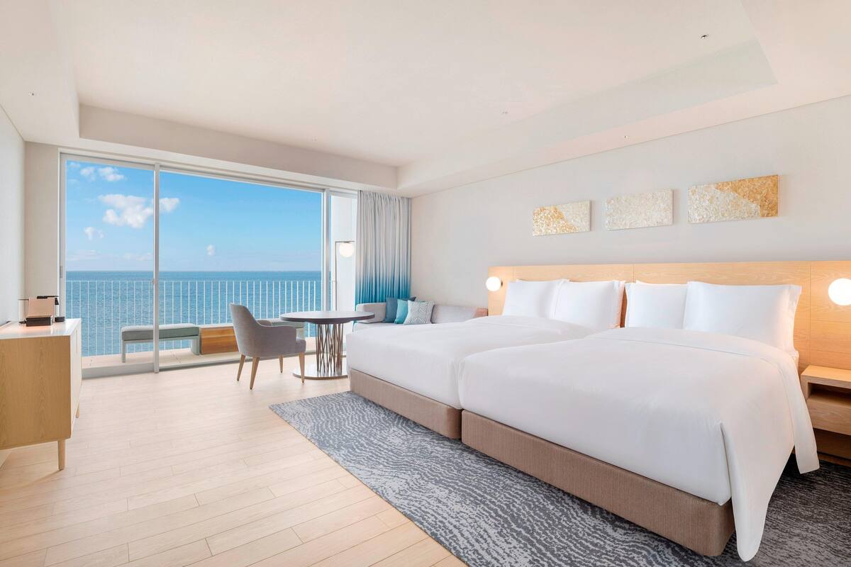 A hotel room with a large bed, a desk, a chair, and a view of the ocean.