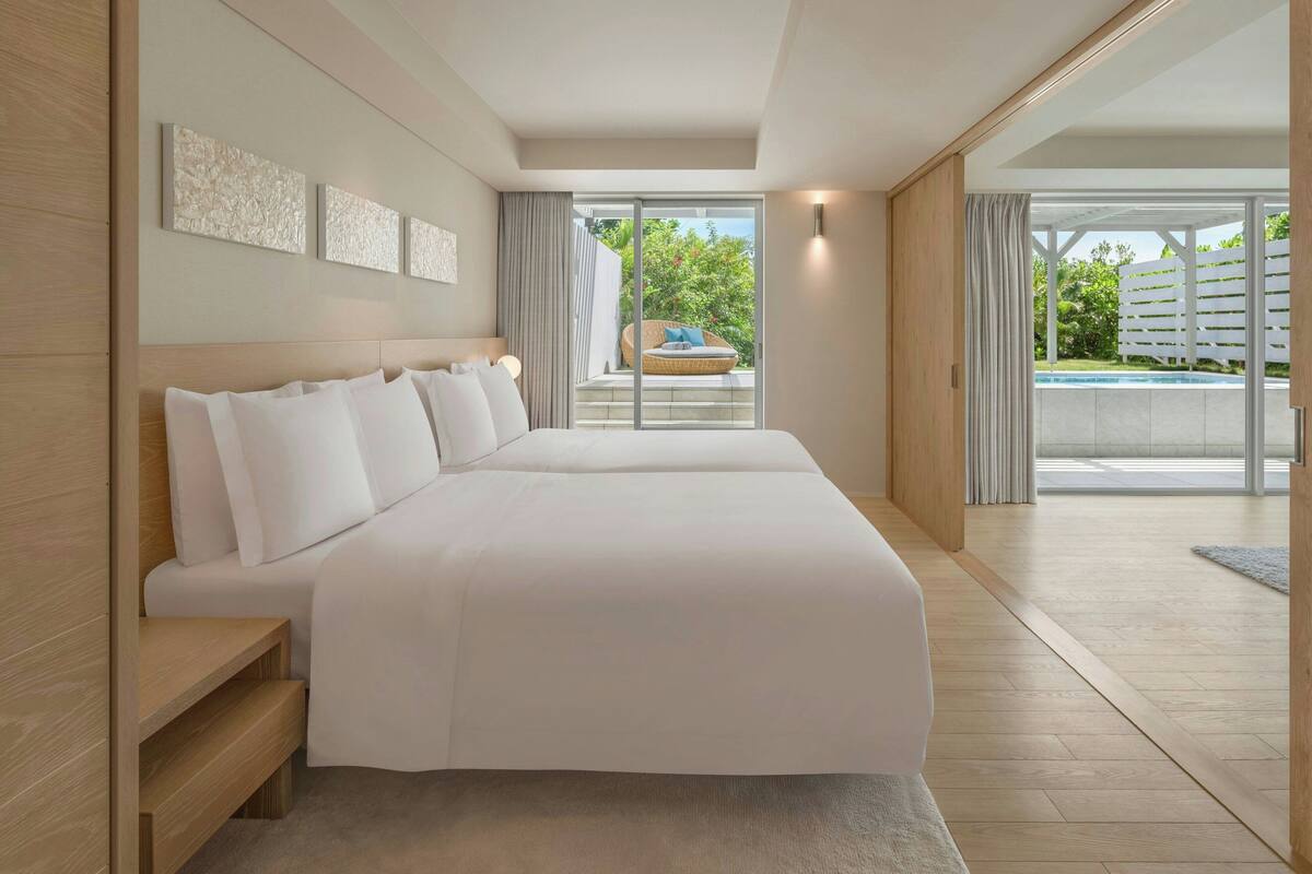 A modern hotel room with a large bed, a wooden bench, and a view of a pool and outdoor area.