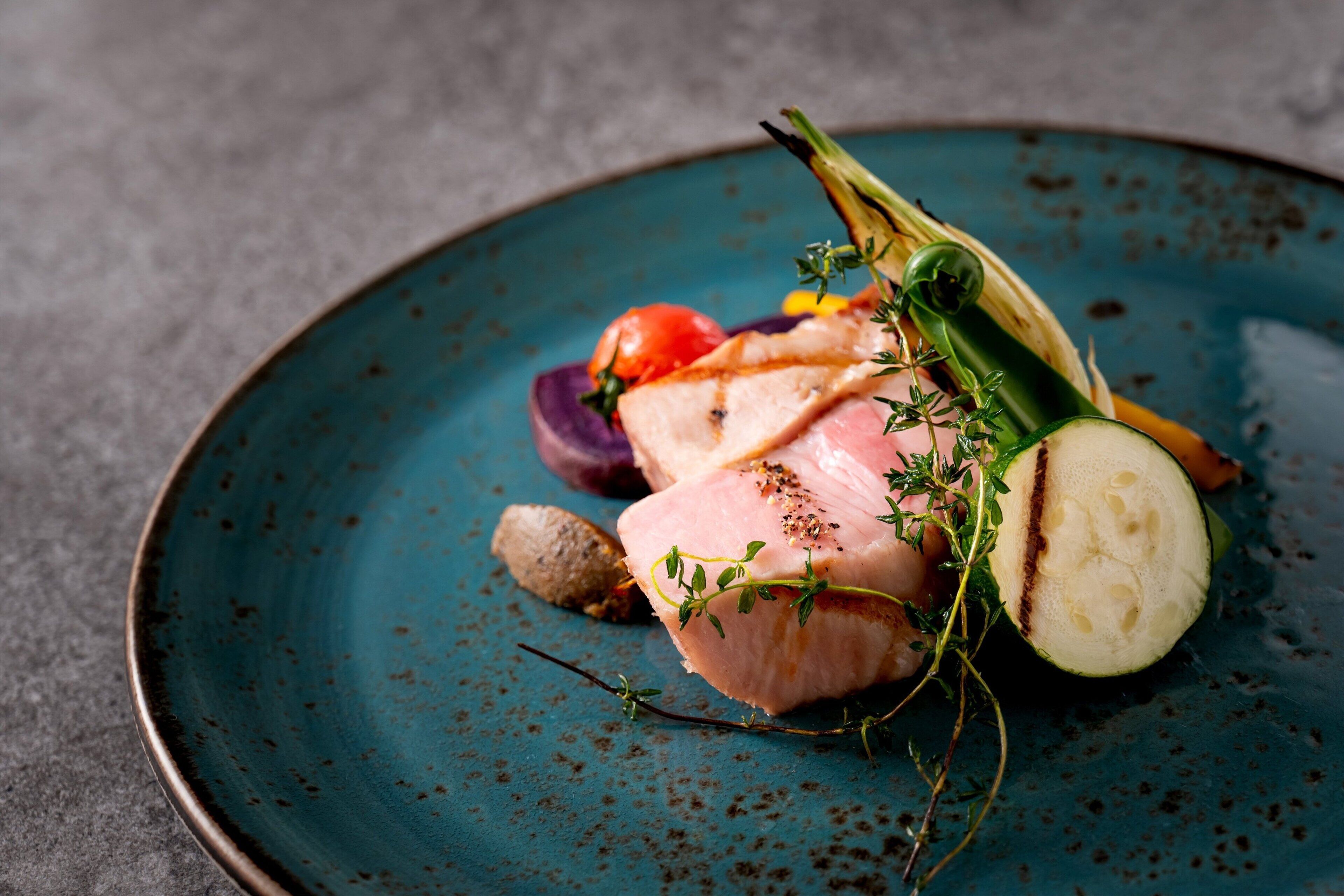 A plate with a piece of meat, vegetables, and herbs.