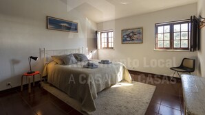 Une chambre à coucher avec un lit, une table de chevet, une chaise et deux fenêtres.