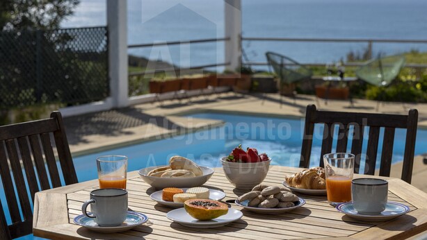Une table avec des aliments pour le petit-déjeuner, un verre de jus d’orange et une vue sur l’océan.