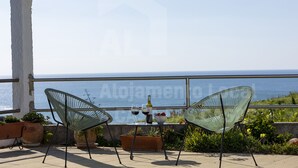 Une terrasse avec deux chaises, une table avec une bouteille de vin et des verres, et une vue sur la mer.