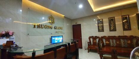 A hotel reception area with a marble reception desk, a digital display, and a traditional wooden sofa.