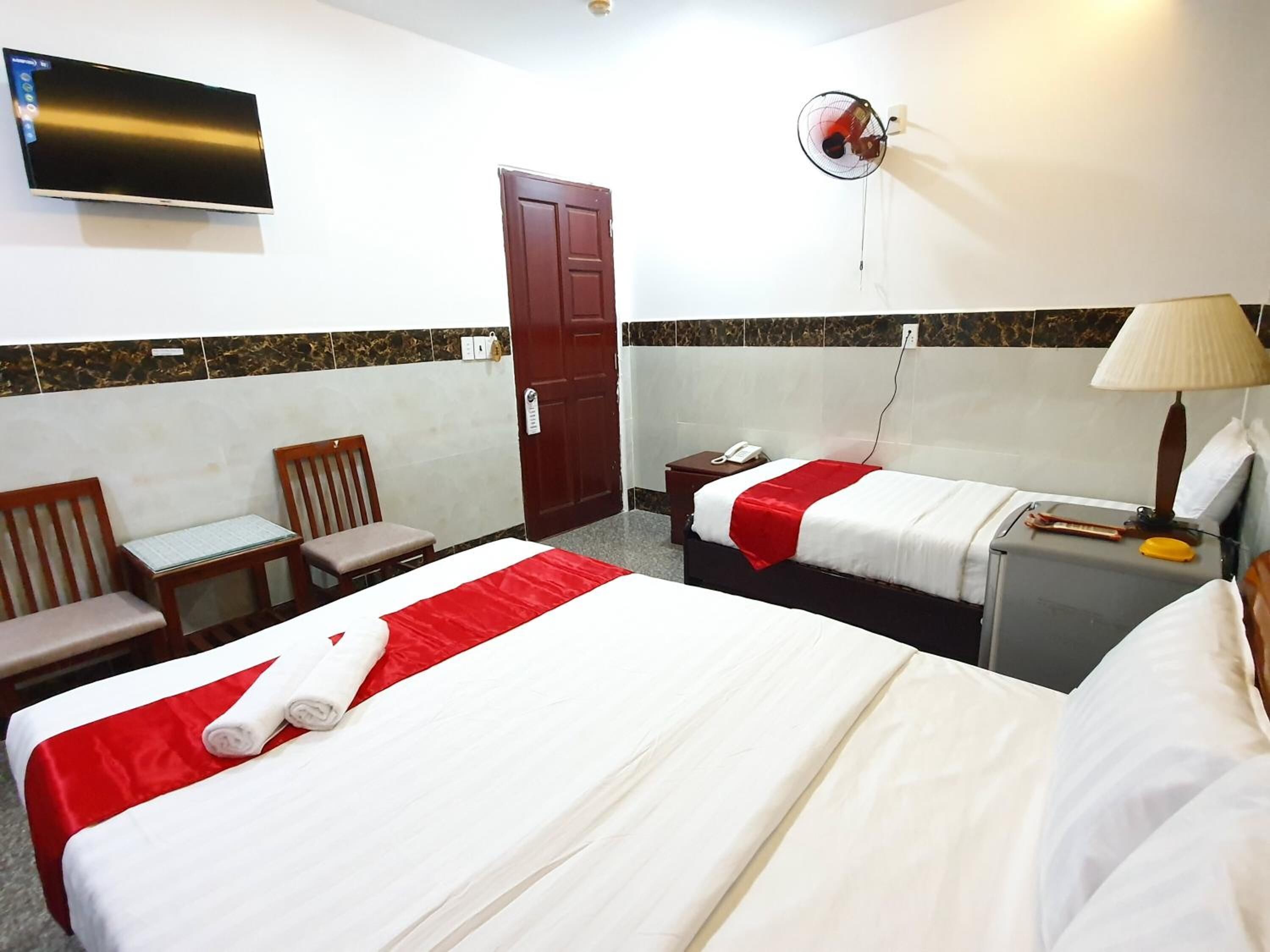 A hotel room with two beds, a TV, a fan, a desk, and a chair.