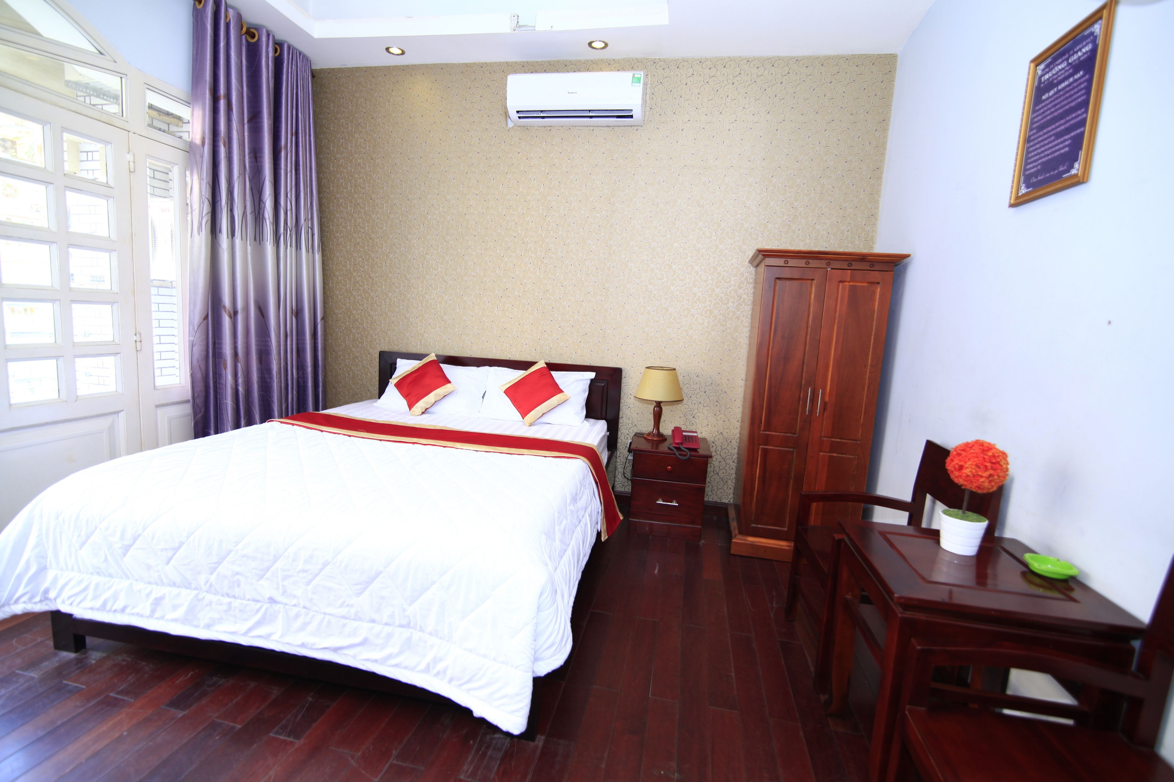A hotel room with a bed, a nightstand, a desk, a chair, a cabinet, and a window with curtains.