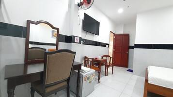 Una habitación de hotel con cama, escritorio con silla, refrigerador pequeño, televisión montada en la pared y una puerta.