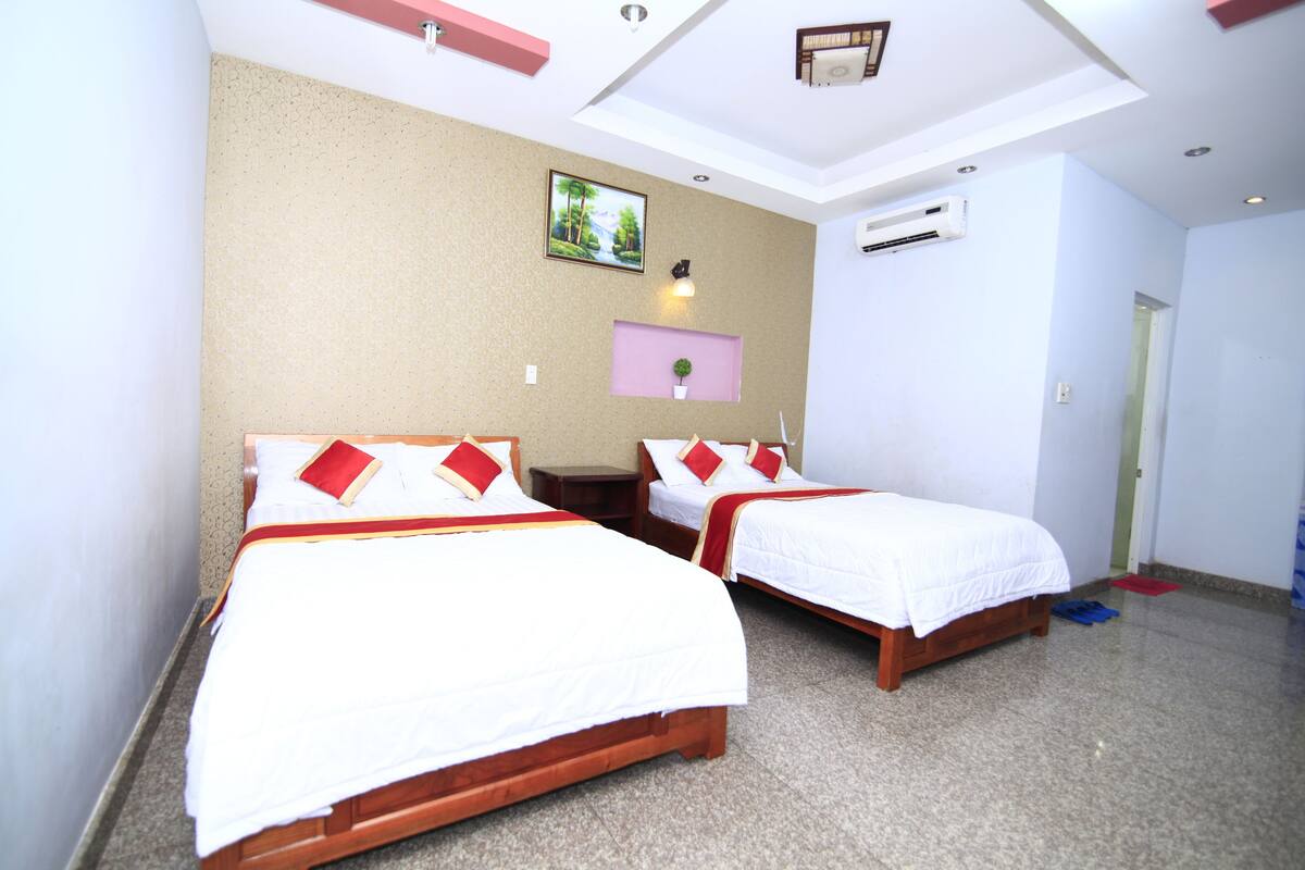 Habitación de hotel con dos camas individuales, una mesita, aire acondicionado de pared y un cuadro en la pared.