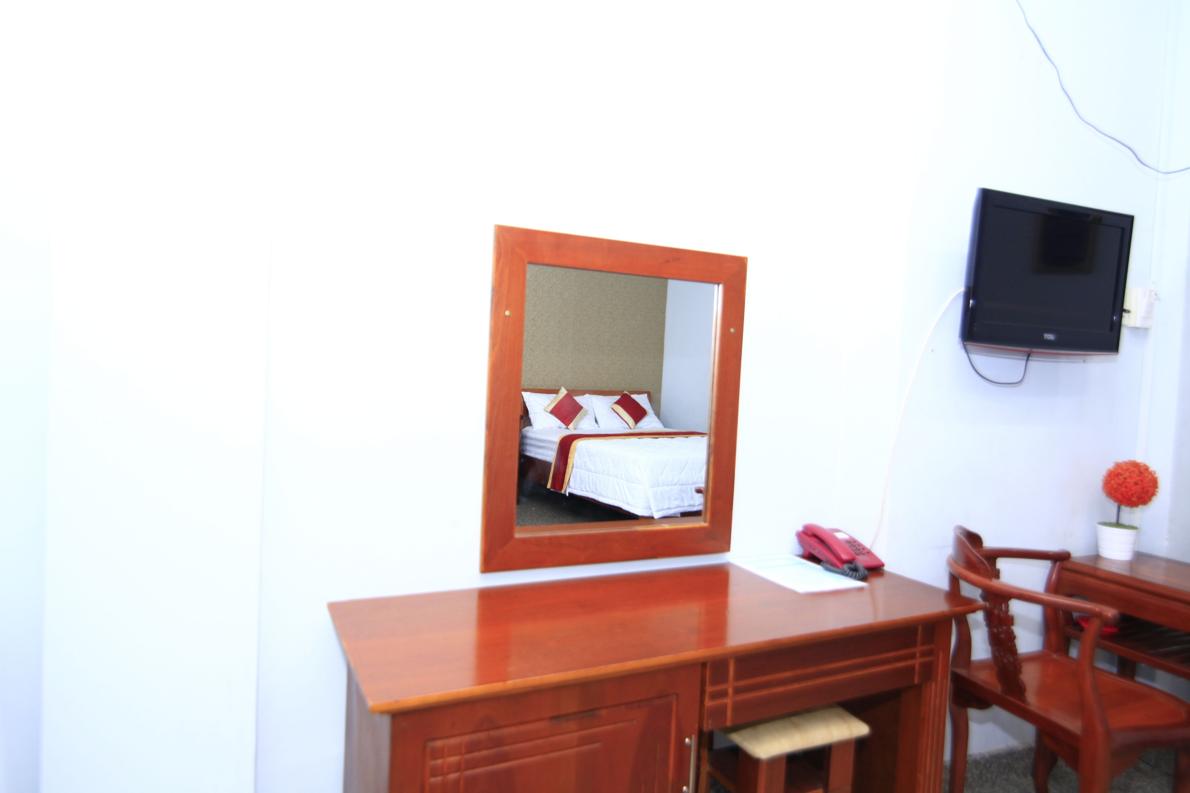 A hotel room with a wooden desk, a chair, a TV mounted on the wall, and a bed with red and white bedding.