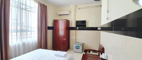 Una habitación de hotel con una cama, un armario de madera, un refrigerador pequeño, un televisor y un escritorio con una silla.