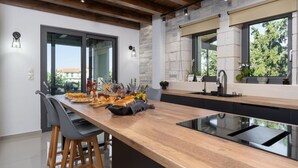 Uma cozinha moderna com bancada de madeira, banquetas pretas, fogão embutido e parede de destaque em pedra.