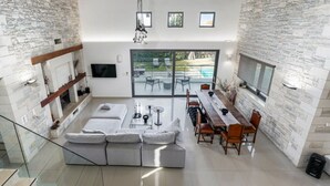 Uma sala de estar ampla com lareira de pedra, sofá, mesa de jantar com cadeiras e uma grande porta de vidro deslizante que dá para um pátio externo.