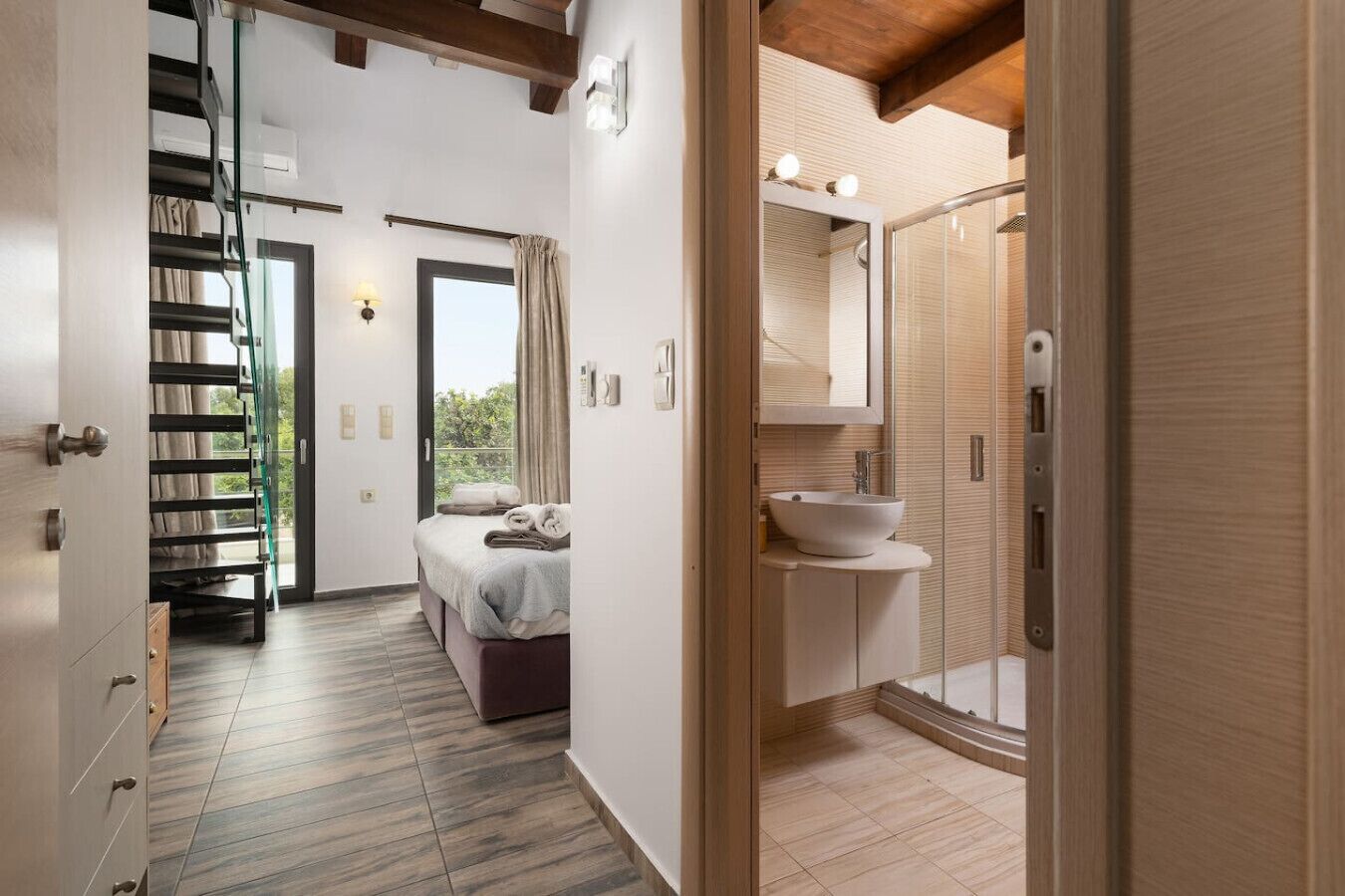 A modern hotel room with a bed, a bathroom with a sink and mirror, and a staircase leading to an outdoor area.