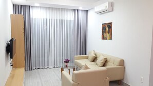 Een moderne woonkamer met een beige bank, een glazen salontafel en een schilderij aan de muur.