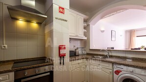 A kitchen with white cabinets, a stainless steel range hood, a built-in oven, a washing machine, and a sink. - Ericeira Beach by ACasaDasCasas (Ericeira)