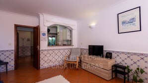A living room with a TV, a sofa, a chair, a small table, and a plant. - Ericeira Beach by ACasaDasCasas (Ericeira)