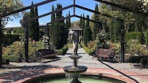Un jardin aménagé, partiellement abrité, avec une fontaine centrale, entouré de bancs et de haies bien entretenues.