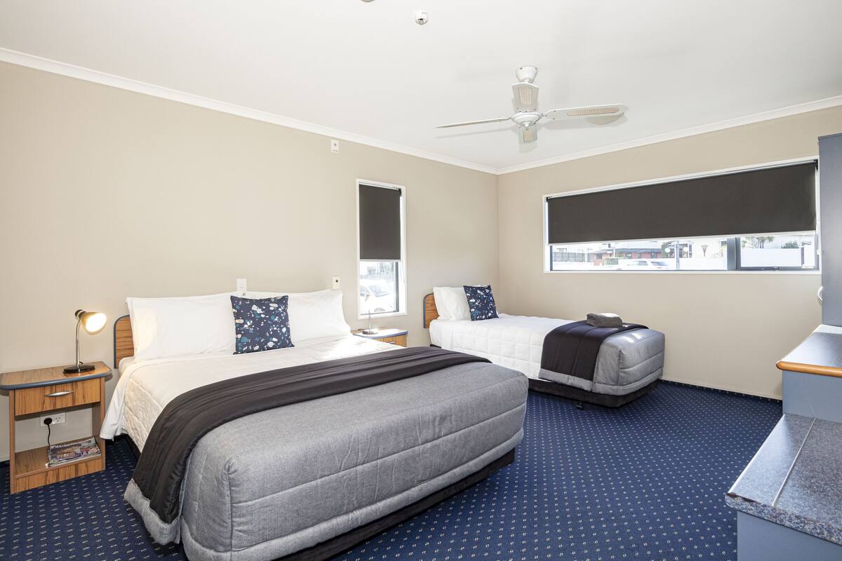 A hotel room with two beds, a desk, a ceiling fan, and a window with a view.