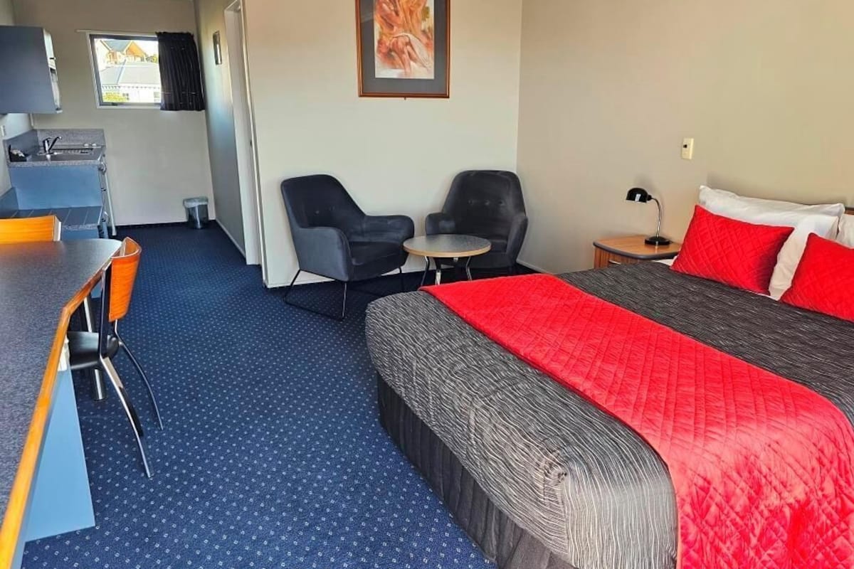 A hotel room with a bed, a desk, two chairs, a small table, a sink, and a window.