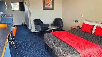 A hotel room with a bed, a desk, two chairs, a small table, a sink, and a window.