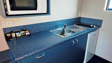 A compact kitchen with a microwave, sink, and a set of Twinings tea tins.