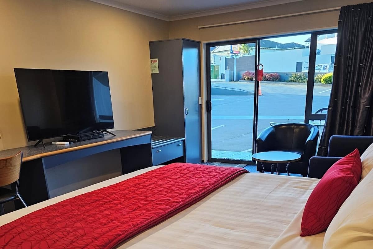 A hotel room with a bed, a TV, a desk, and a view of the street.