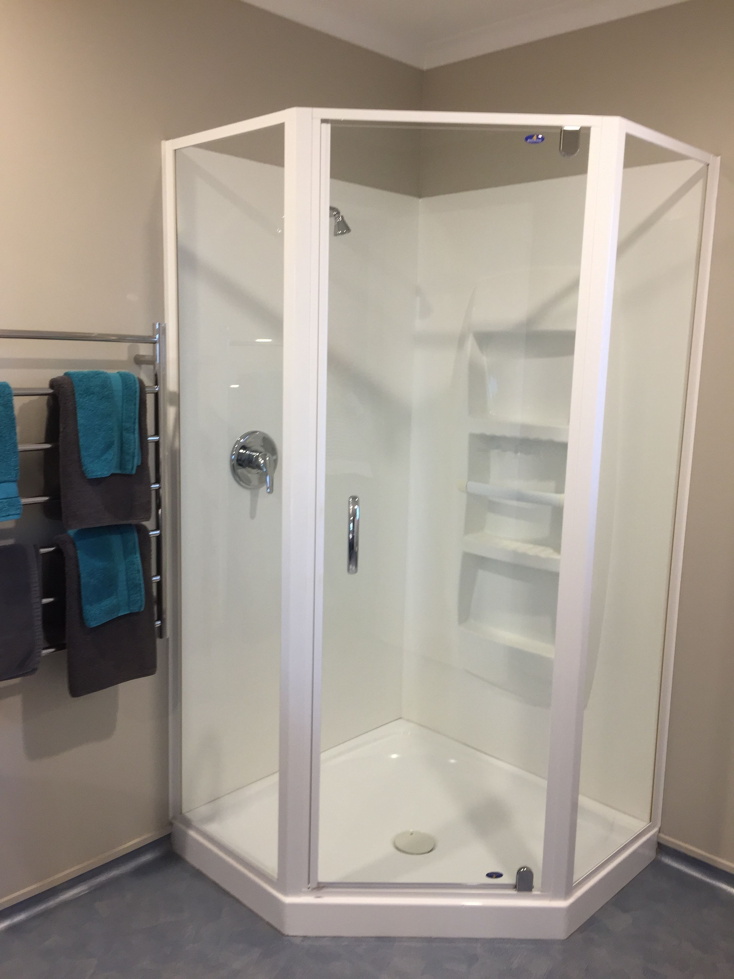 A corner shower with a glass door, a chrome handle, and a shelf inside.