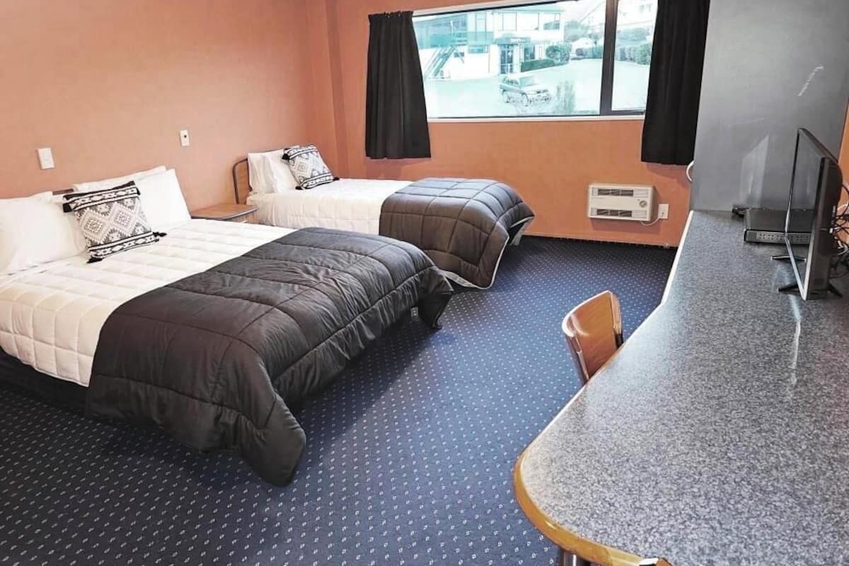 A hotel room with two beds, a desk, and a chair.