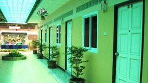 A corridor with a tiled floor, potted plants, and doors on one side. - All Day Hotel (Nong Khai)