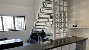 A modern kitchen with a black countertop, a spiral staircase with glass panels, and a view of tall buildings outside.