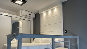 A modern bedroom with a bed, a white air conditioning unit, a built-in wardrobe, and a bedside table.