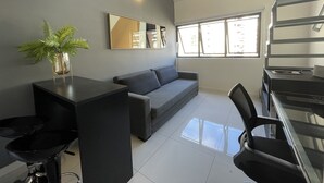 A modern living room with a grey sofa, a black coffee table, a black chair, a small plant, and a large mirror on the wall.