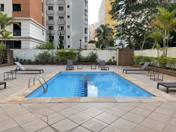 Une piscine rectangulaire dont les bords sont recouverts de carreaux, entourée de chaises longues et d’un petit muret en briques.
