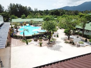 A resort with a central swimming pool, surrounded by palm trees and a mountainous backdrop. - Walking Street Hostel by New Wave - Adults Only (Koh Lipe)