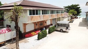 Un edificio de dos pisos con techo de tejas, un espacio de estar al aire libre cubierto con sombrillas, y una camioneta estacionada.