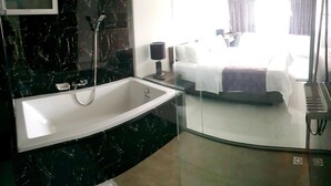Un baño moderno con una bañera grande, cabina de ducha de cristal y una mesita de noche con lámpara.