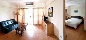 A hotel room with a bed, a sofa, a TV, a desk, and a window with curtains. - Walking Street Hostel by New Wave - Adults Only (Koh Lipe)