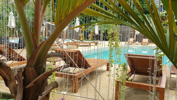 Zona de piscina con sillones de madera y una piscina azul cristalina.