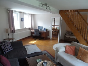 A living room with a sofa, a coffee table, a desk with a computer, and a staircase. - 5 bedrooms, quiet town location, garden, 2 parking spaces, 200m to market square (Goslar)
