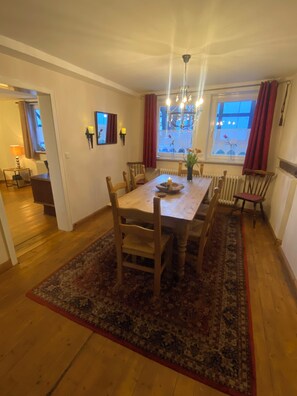 A dining area with a wooden table, chairs, a chandelier, and a view of the street outside. - 5 bedrooms, quiet town location, garden, 2 parking spaces, 200m to market square (Goslar)