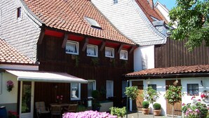 Ein traditionelles Haus im europäischen Stil mit Ziegeldach, einer überdachten Terrasse und einem gepflegten Garten mit Blumen und Sträuchern.